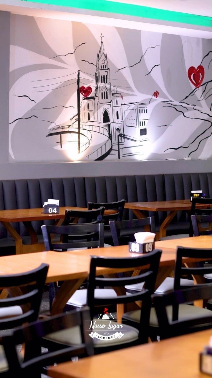 Salão do Nosso Lugar com mesas de madeira e mural desenhado na parede