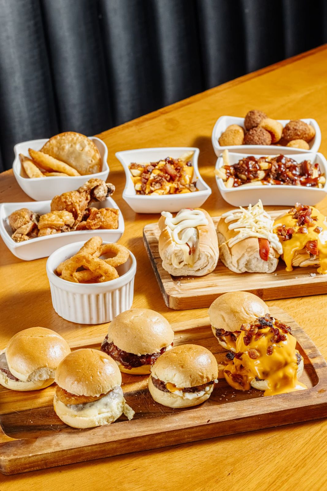 Mesa com mini burgers, mini hot dogs, fritas, bolinhos, torresmo e anéis de cebola